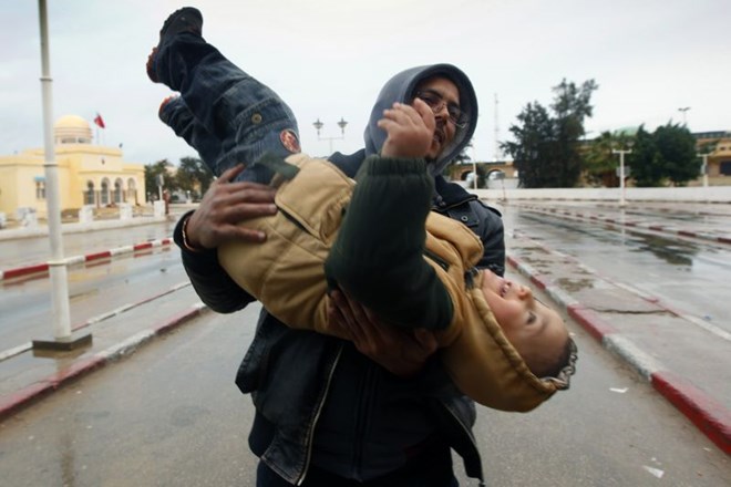 Moški nosi dečka čez mejo iz Libije v Tunizijo. Na tisoče ljudi beži pred ekstremnim nasiljem v Libiji.