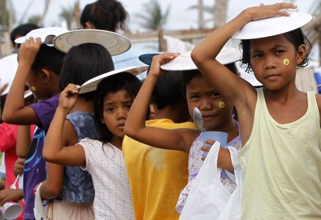 Filipinski otroci si s krožniki pred dežjem ščitijo glave, medtem ko v vrsti čakajo na brezplačen obrok, ki jih delijo v...