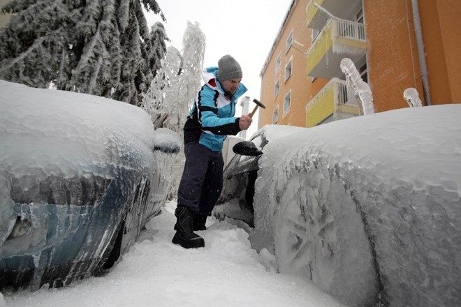 Moški v Postojni s kladivom čisti led s svojega avtomobila. 