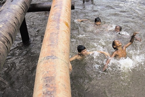 Ekvadorski otroci  se kopajo pod naftovodom, ki je spuščal nafto in strupe.