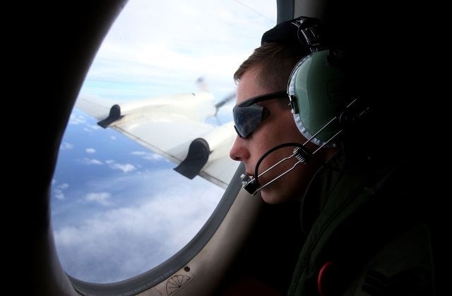 Moški skozi okno opreza za morebitnimi ostanki pogrešanega letala. 