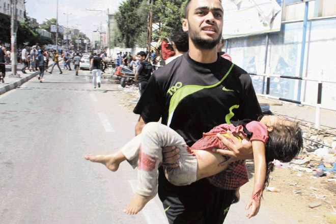 Moški nosi otroka, ki je bil med zračnimi napadi izraelske vojske ubit v eksploziji pred šolskim poslopjem Združenih narodov,...