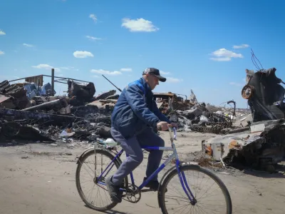 A local residence rides a bike past a destroyed Russian military vehicle in Bucha, on the outskirts of Kyiv, Ukraine, Tuesday, May 10, 2022. (AP Photo/Efrem Lukatsky)