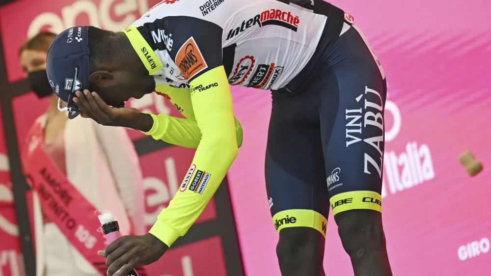 Eritrea's Biniam Girmay touches his eye after spraying sparkling wine on the podium to celebrate winning the 10th stage of the Giro D'Italia cycling race from Pescara to Jesi, Italy, Tuesday, May 17, 2022. Girmay was then taken to a local hospital after getting injured when he popped a champagne cork into his eye during the podium celebration. (Massimo Paolone/LaPresse via AP)