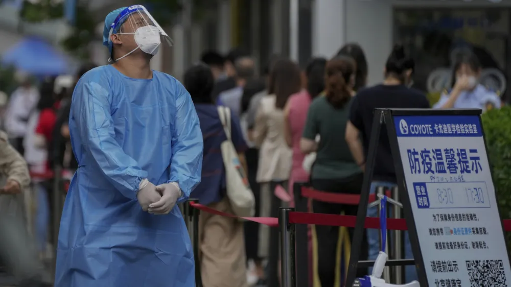 A worker in protective gears reacts as residents line up at a testing site due to requirements for a negative COVID test in the last 72 hours to enter some buildings and using public transportation in Beijing, Monday, July 4, 2022. (AP Photo/Andy Wong)