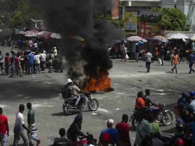 People walk around burning tires set up by taxi drivers to protest the country's fuel shortage in Port-au-Prince, Haiti, Wednesday, July 13, 2022. (AP Photo/Odelyn Joseph)