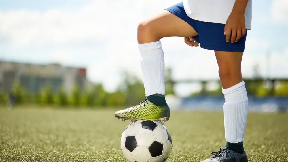 Side view portrait of unrecognizable young sportsman standing in football field with leg on ball