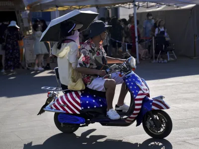 A Chinese couple ride on an electric bike with decals of the American flag, passing by visitors waiting in line to board a ferry at Erhai lake in Dali, in southwestern China's Yunnan province on Saturday, July 16, 2022. Treasury Secretary Janet Yellen said Tuesday the U.S. and South Korea should deepen their trade ties to avoid letting other countries use their market positions to unfair advantage — calling out China by name. (AP Photo/Andy Wong)