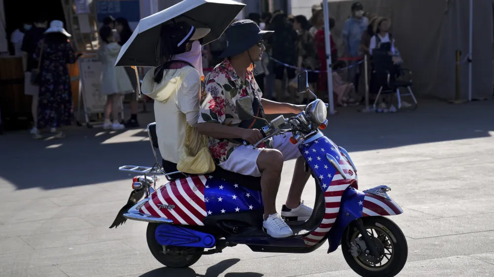 A Chinese couple ride on an electric bike with decals of the American flag, passing by visitors waiting in line to board a ferry at Erhai lake in Dali, in southwestern China's Yunnan province on Saturday, July 16, 2022. Treasury Secretary Janet Yellen said Tuesday the U.S. and South Korea should deepen their trade ties to avoid letting other countries use their market positions to unfair advantage — calling out China by name. (AP Photo/Andy Wong)