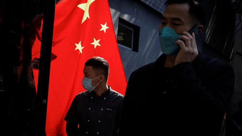 People wearing masks walk past a Chinese national flag as outbreaks of coronavirus disease (COVID-19) continue in Beijing, China, November 3, 2022. REUTERS/Thomas Peter
