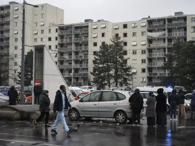 Onlookers stand next to apartment buildings seen in background at Le Mas du Taureau neighborhood, in Vaulx en Velin, outside Lyon, central France, Friday, Dec. 16, 2022. French authorities say 10 people including five children died in a fire in an apartment building outside the city of Lyon. The cause of the fire is being investigated. (AP Photo/Laurent Cipriani)