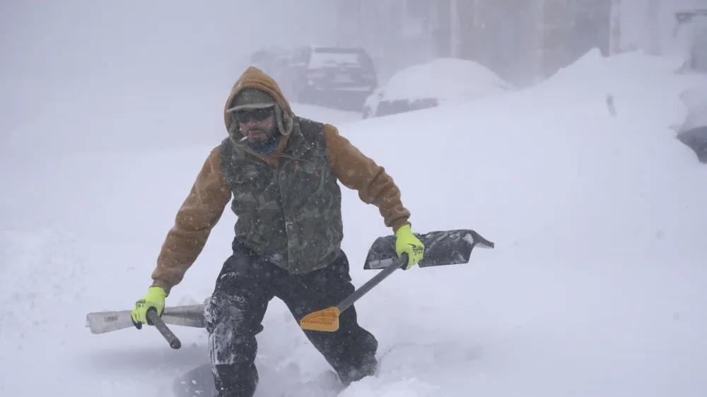 Travis Sanchez trudges over a snowdrift with a pair of shovels for a stranded motorist on Chenango Street in Buffalo, N.Y. on Saturday, Dec. 24, 2022. (Derek Gee/The Buffalo News via AP)