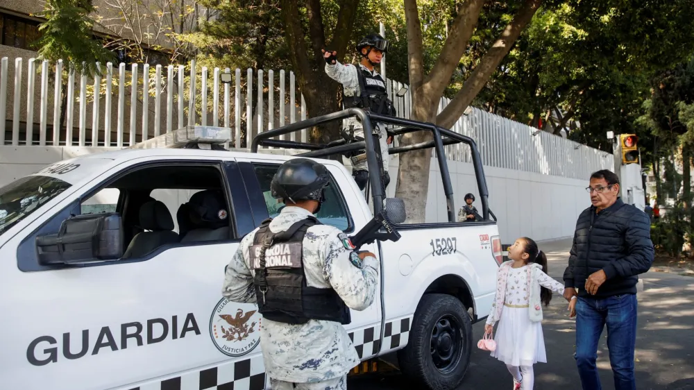 A man and a girl pass by as members of the National Guard keep watch following the detention of Mexican drug gang leader Ovidio Guzman, a son of incarcerated kingpin Joaquin "El Chapo" Guzman, who has been arrested by Mexican authorities, outside the building of the Attorney General's Office for Special Investigations on Organized Crime (FEMDO), in Mexico City, Mexico January 5, 2023. REUTERS/Raquel Cunha