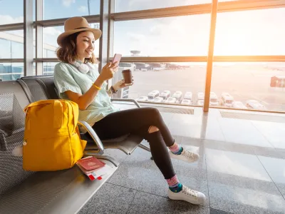 Happy asian woman waiting for her airplane in airport with passport and baggage. Vacation and journey concept