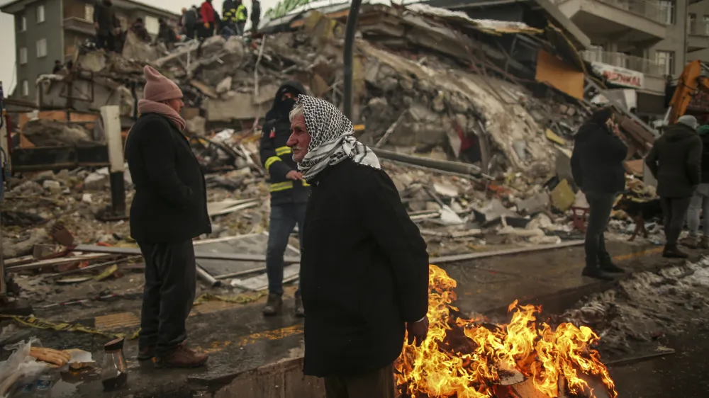 FILE - People warm themselves next to a collapsed building in Malatya, Turkey, on Feb. 7, 2023. A magnitude 5.6 earthquake shook southern Turkey on Monday Feb. 27, 2023 three weeks after a catastrophic temblor devastated the region, causing some already damaged buildings to collapse and killing at least one person, the country's disaster management agency, AFAD, said. (AP Photo/Emrah Gurel, File)