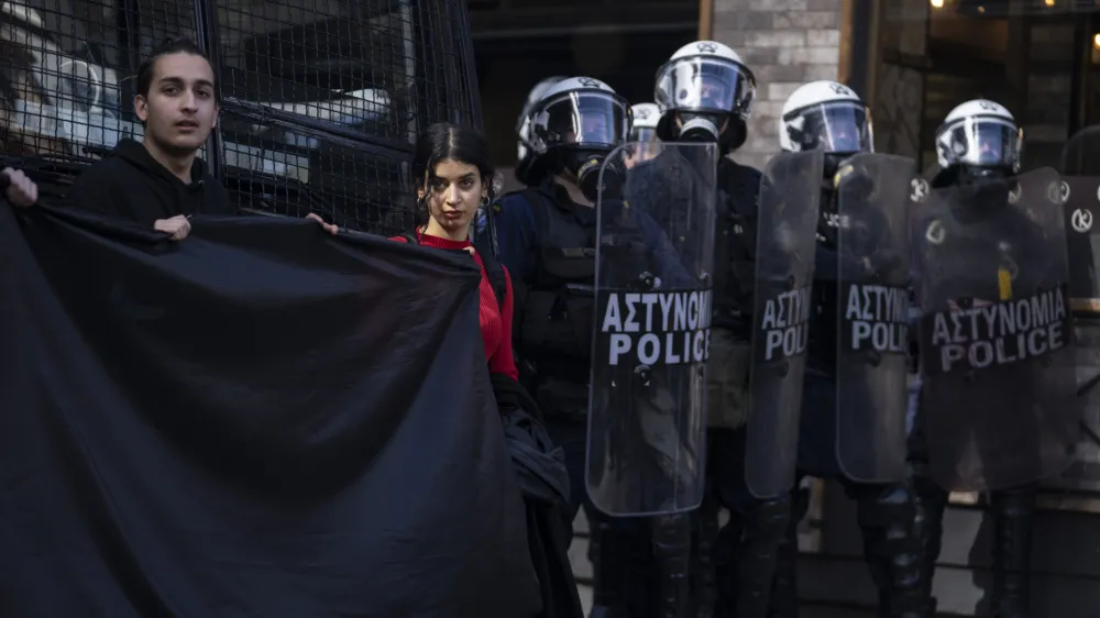 University students hold a black banner as they stand next to riot police quarding the headquarters of private operator Hellenic Train, in Athens, Friday, March 3, 2023. Demonstrators marched through the city center to protest the deaths of dozens of people late Tuesday, in Greece's worst recorded rail accident. (AP Photo/Petros Giannakouris)