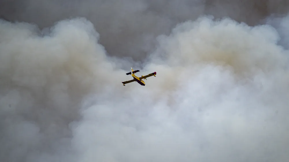 Smoke raises from a forest fire burning below as a firefighting plane flies over San Agustin, Spain on Friday March 24, 2023 Hundreds of people were evacuated as a major forest fire raged in Spain's eastern Castellon region on Friday, marking the early start to the nation's fire season amid bone dry conditions. (Lorena Sopena/Europa Press via AP)