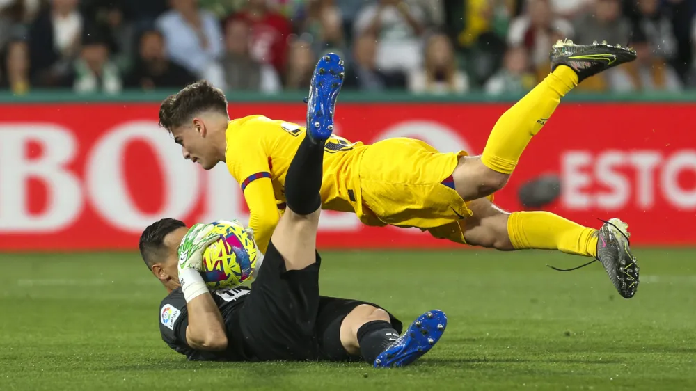Elche's goalkeeper Edgar Badia, left, makes a save in front of Barcelona's Gavi during a Spanish La Liga soccer match between Elche and Barcelona, at the Martinez Valero Stadium in Elche, Spain, Saturday, April 1, 2023. (AP Photo/Alberto Saiz)