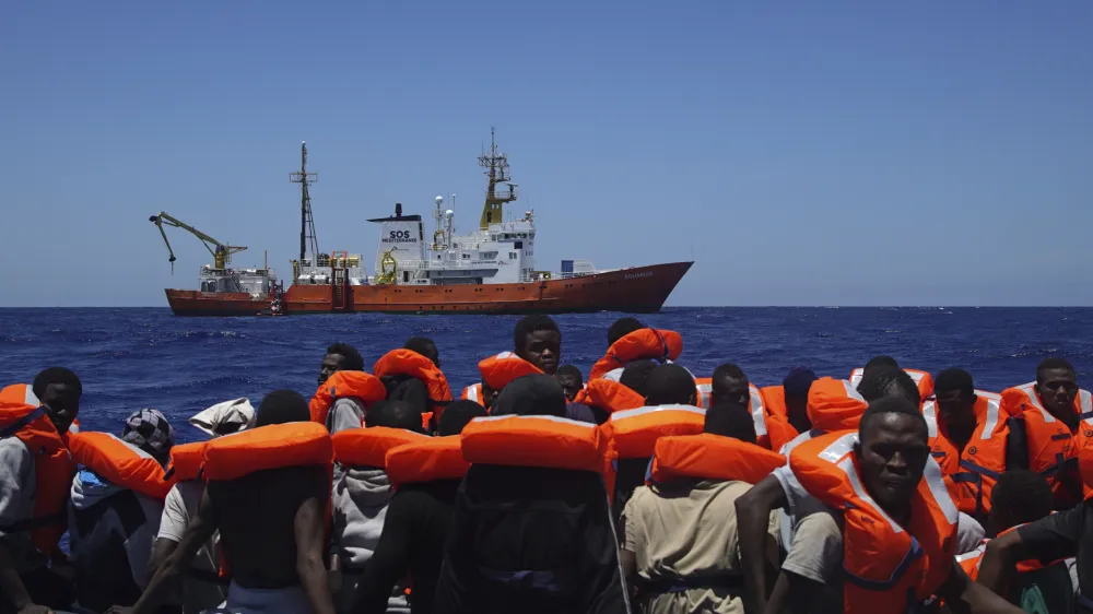 ﻿FILE - In this Thursday June 23, 2016 file photo, Migrants aboard a dinghy in the Mediterranean Sea wait to be rescued by members of the aid group Medecins Sans Frontieres (MSF) and the rescue group SOS Mediterranee Rescuers of SOS Mediterranee. Doctors Without Borders said Saturday, Aug. 12, 2017, it is temporarily suspending the activity of its rescue ship due to alleged threats from Libyaâ€™s coast guard, which has increasingly become more aggressive in patrolling the waters off its coasts where human traffickers launch boats crowded with migrants desperate to reach Europe. (AP Photo/Bram Janssen, File)
