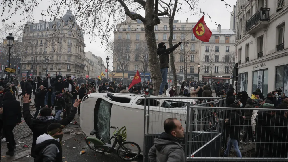 A demonstrator waves a Kurdistan Workers Party, PKK, flag as he stands on an over turn car during a protest against the recent shooting at the Kurdish culture center in Paris, Saturday, Dec. 24, 2022. Kurdish activists, left-wing politicians and anti-racism groups are holding a protest Saturday in Paris after three people were killed at a Kurdish cultural center in an attack aimed at foreigners.(AP Photo/Lewis Joly)