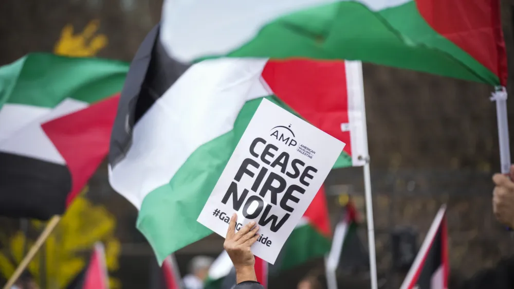 A person holds a sign as others wave flags during a march calling for a ceasefire in Gaza at the Washington Monument, Saturday, Oct. 21, 2023, in Washington. (AP Photo/Andrew Harnik)