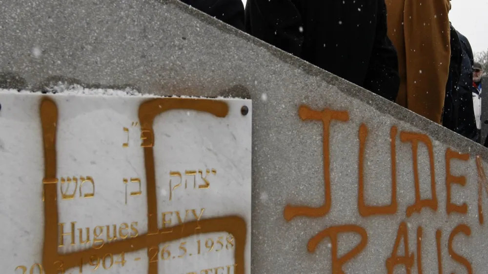 France's Interior Minister Brice Hortefeux (R) walks next to a tombstone desecrated by vandals with a Nazi swastika and the slogan "Jews out" in the Jewish Cemetery of Cronenbourg near Strasbourg January 28, 2010. Thirty-one tombs were found desecrated on Wednesday in the Jewish cemetery of Cronenbourg, the biggest Jewish cemetery of Strasbourg. REUTERS/Vincent Kessler (CRIME LAW RELIGION POLITICS)