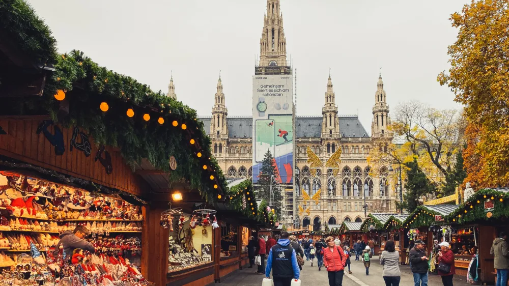Vienna, Austria - November 20, 2019: Austrian Christmas huts, vendor retailing colorful baubles and craft toys. Bazaar sale in evening time. Magical celebration atmosphere. People shopping traditional gifts.