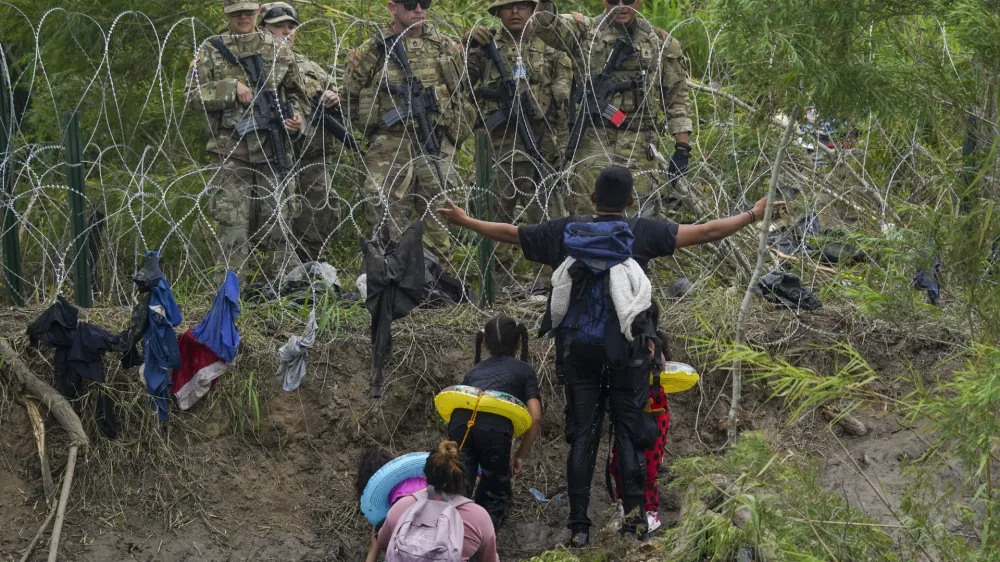 FILE - A migrant gestures to Texas National Guards standing behind razor wire on the bank of the Rio Grande river, seen from Matamoros, Mexico, May 11, 2023. (AP Photo/Fernando Llano, File)