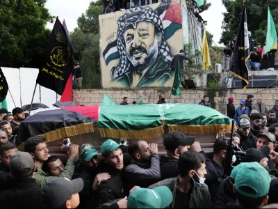 Mourners carry the coffin of Saleh Arouri, one of the top Hamas commanders, who was killed in an apparent Israeli strike Tuesday, as they pass in front of a graffiti that shows late Palestinian leader Yasser Arafat, during his funeral in Beirut, Lebanon, Thursday, Jan. 4, 2024. (AP Photo/Hussein Malla)