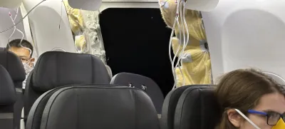 This image provided by Kelly Bartlett shows passengers near a hole in the fuselage of an Alaska Airlines Boeing 737 Max 9, Flight 1282, which was forced to return to Portland International Airport on Friday, Jan. 5, 2024. (Kelly Bartlett via AP)