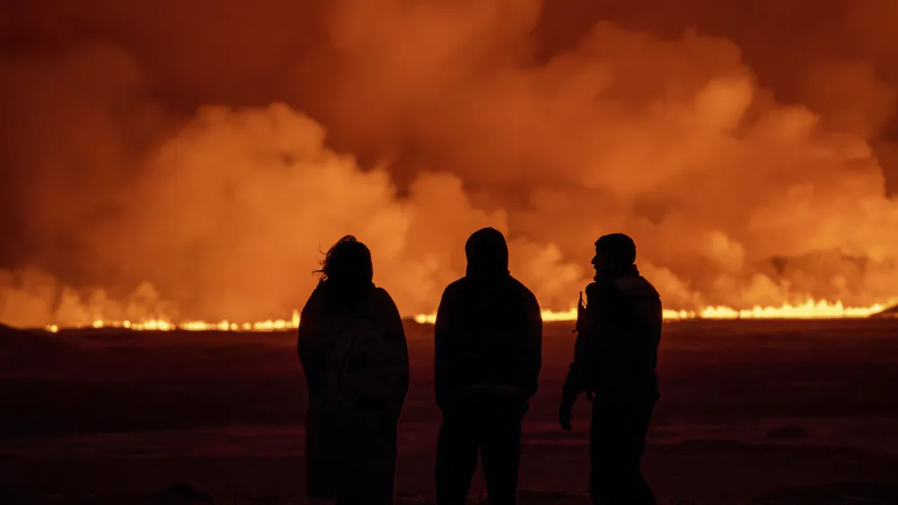 People watch as the night sky is illuminated caused by the eruption of a volcano in Grindavik on Iceland's Reykjanes Peninsula, Monday, Dec. 18, 2023. (AP Photo/Marco Di Marco)