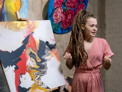 Young female auctioneer or speaker with dreadlocks describing abstraction illustrated on painting in front of audience
