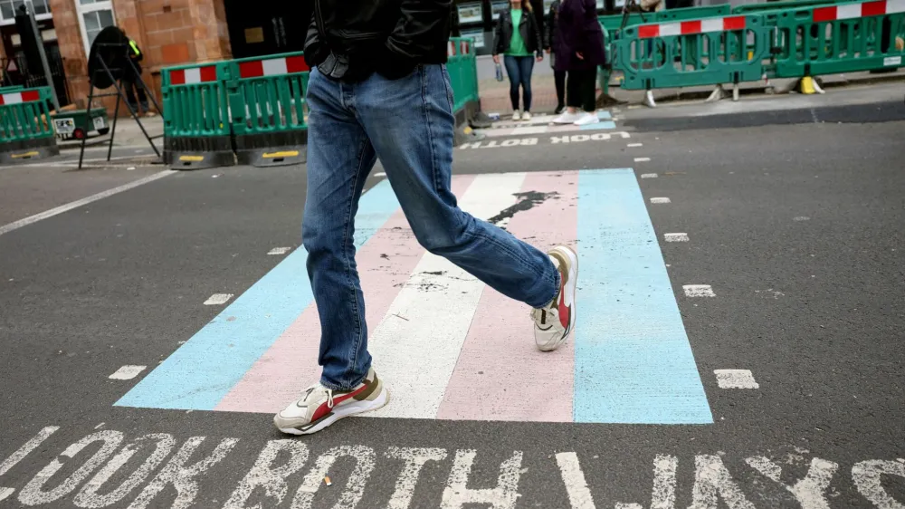 A person walks on a pedestrian crossing decorated with the pattern of the transgender flag on a street in London, Britain, April 10, 2024. REUTERS/Isabel Infantes