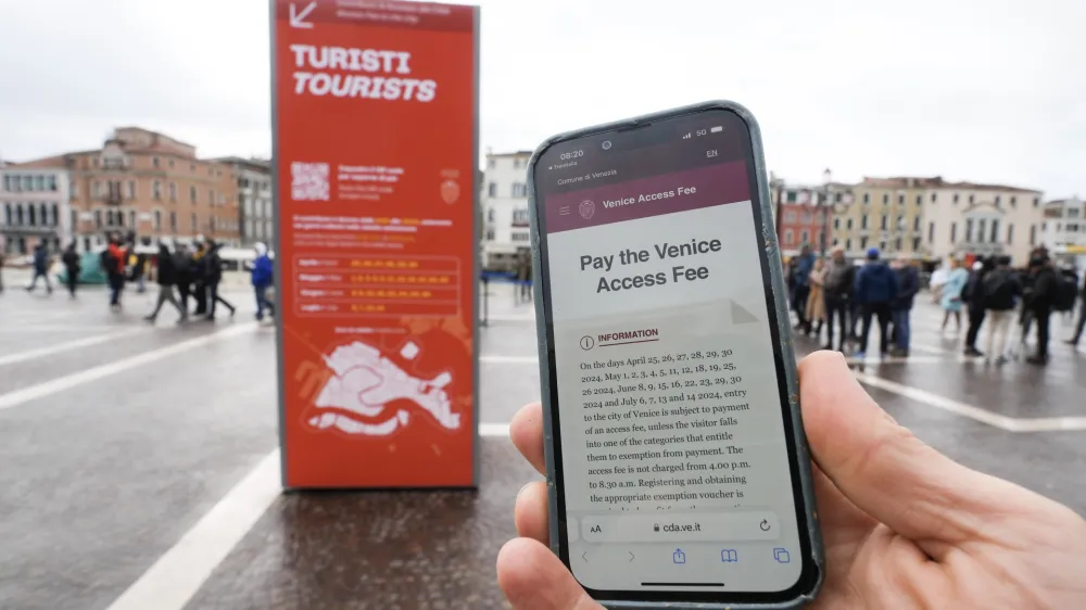 A tourist shows a QR code fee access outside the main train station in Venice, Italy, Thursday, April 25, 2024. The fragile lagoon city of Venice begins a pilot program Thursday to charge daytrippers a 5 euro entry fee that authorities hope will discourage tourists from arriving on peak days. The daytripper tax is being tested on 29 days through July, mostly weekends and holidays starting with Italy's Liberation Day holiday Thursday. Officials expect some 10,000 people will pay the fee to access the city on the first day, downloading a QR code to prove their payment, while another 70,000 will receive exceptions, for example, because they work in Venice or live in the Veneto region. (AP Photo/Luca Bruno)