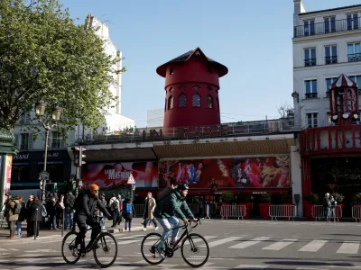 Cyclists pass by the landmark red windmill atop the Moulin Rouge, Paris' most famous cabaret club, after its sails fell off during the night in Paris, France, April 25, 2024. REUTERS/Benoit Tessier