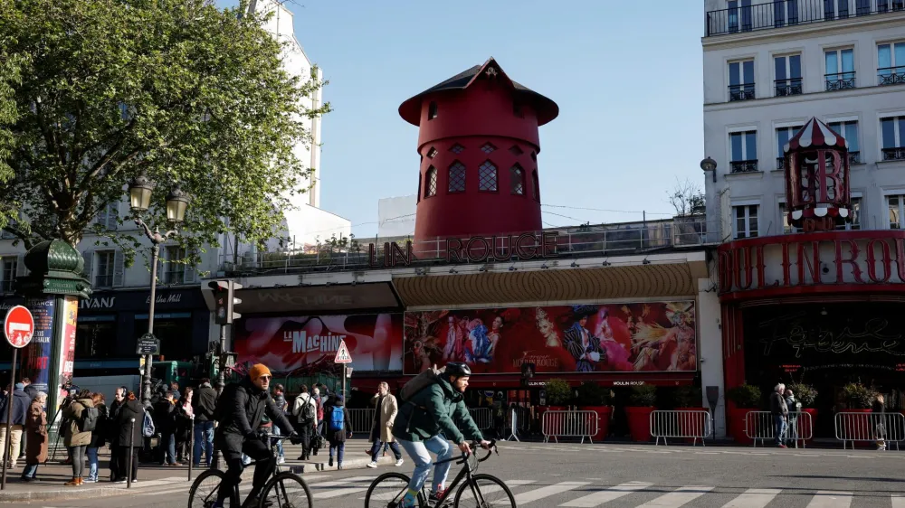 Cyclists pass by the landmark red windmill atop the Moulin Rouge, Paris' most famous cabaret club, after its sails fell off during the night in Paris, France, April 25, 2024. REUTERS/Benoit Tessier