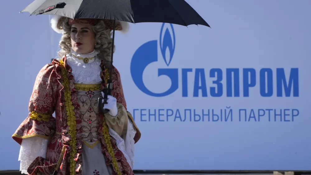 An actor wearing XVIII century dress walks past a logo of Russian gas monopoly Gazprom in St. Petersburg, Russia, Friday, May 27, 2022. (AP Photo/Dmitri Lovetsky)