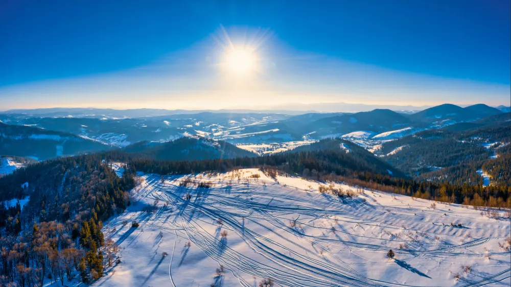 Top view of a beautiful mesmerizing view of the ski slope with ski trails located in the mountains on a sunny winter frosty evening. Vacation and tourism concept in winter. Copyspace