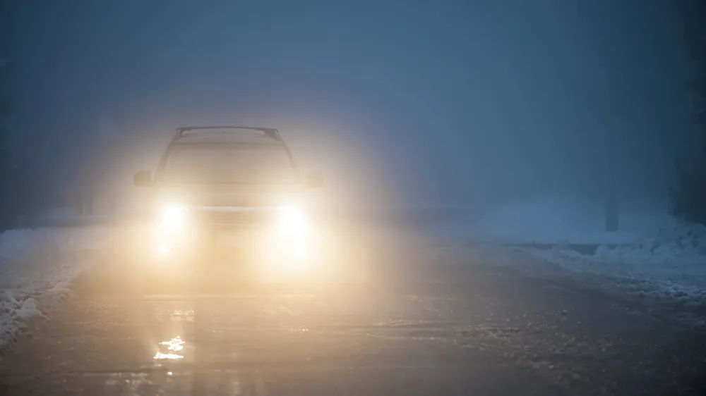 Bright headlights of a car driving on foggy winter road