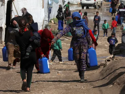 FILE PHOTO: Syrian refugees walk as they carry containers at an informal tented settlement in the Bekaa valley, Lebanon March 12, 2021. Picture taken March 12, 2021. REUTERS/Mohamed Azakir/File Photo