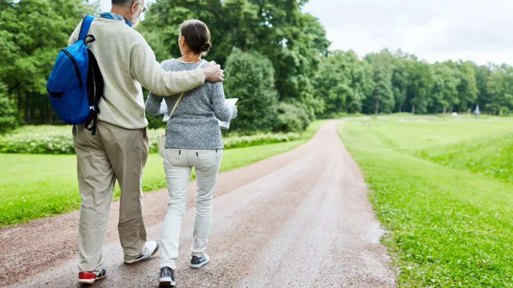 ﻿Affectionate retired backpackers moving down country road / Foto: Shironosov