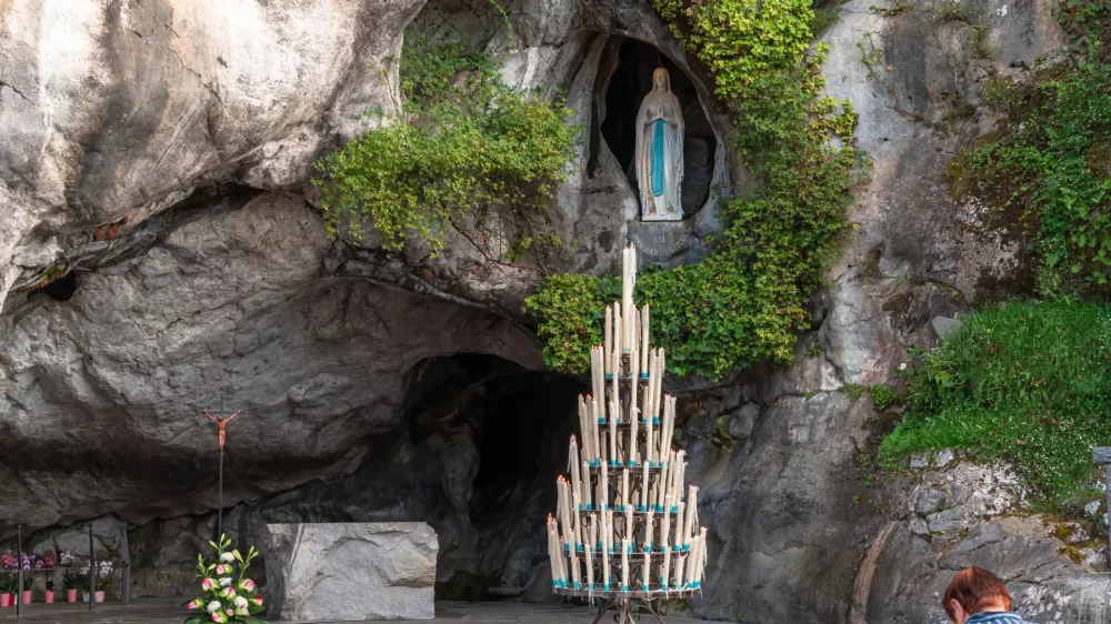 Lourdes, France - August 28, 2021: Woman praying in front of the cave of apparitions of holy Mary in Lourdes