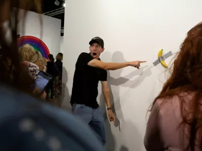 FILE PHOTO: A man poses for a photo next to a banana attached with duct-tape that replaces the artwork 'Comedian' by the artist Maurizio Cattelan, which was eaten by David Datuna, in Miami Beach, Florida, December 7, 2019. REUTERS/Eva Marie Uzcategui/File Photo