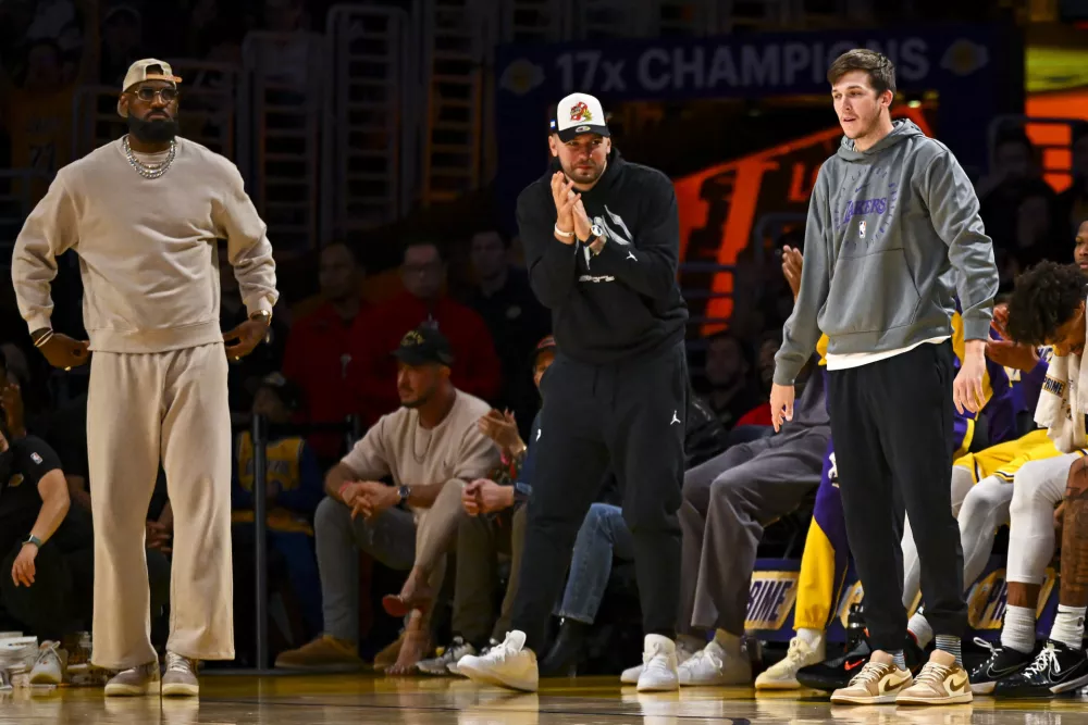 Mar 20, 2025; Los Angeles, California, USA; Los Angeles Lakers forward LeBron James (23), guard Luka Doncic (77), and guard Austin Reaves (15) on the sidelines against the Milwaukee Bucks during the first half at Crypto.com Arena. Mandatory Credit: Jonathan Hui-Imagn Images