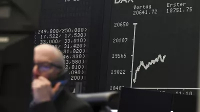 While a stock exchange trader sits in front of his monitors on the trading floor of the Frankfurt Stock Exchange, Germany, the display board with the Dax curve shows a value of less than 20,000 points. (Arne Dedert/dpa via AP)