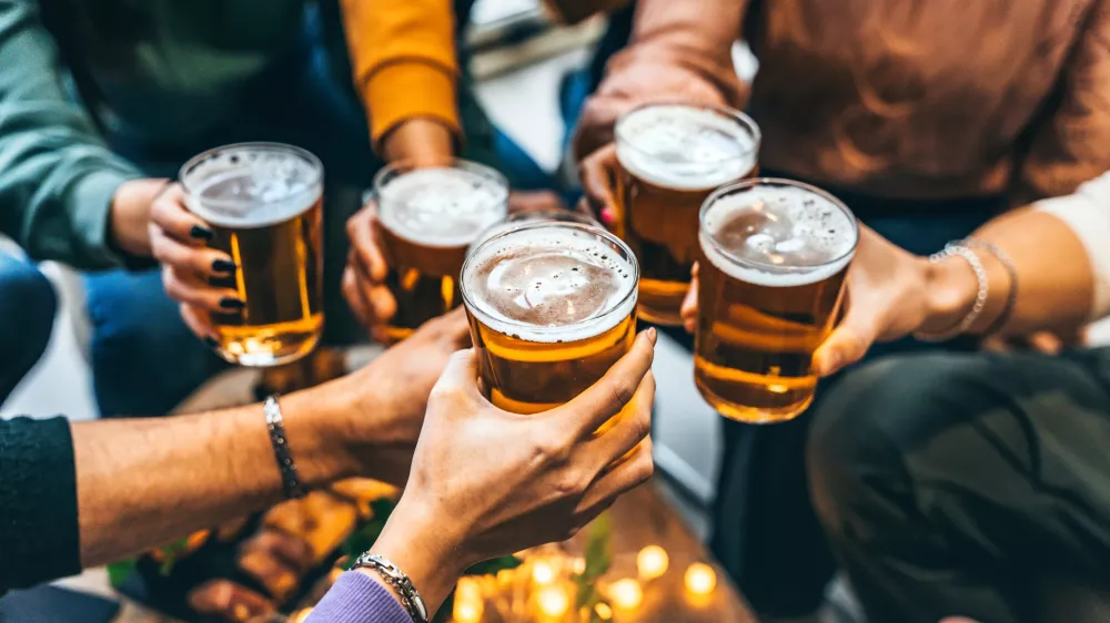 Group of friends drinking and toasting glass of beer at brewery pub restaurant- Happy multiracial people enjoying happy hour with pint sitting at bar table- Youth Food and beverage lifestyle concept / Foto: Nicolas Micolani