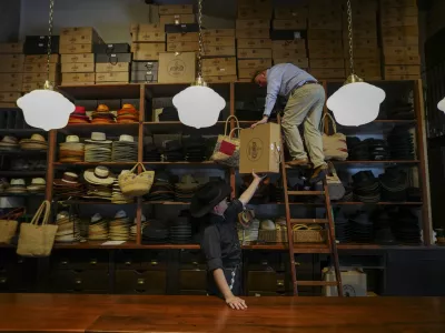 Employees work together to store products on a top shelf at the "Donde Golpea el Monito" hat shop and museum that preserves a hat-making tradition dating back to 1915, in Santiago, Chile, Thursday, April 3, 2025. (AP Photo/Esteban Felix)