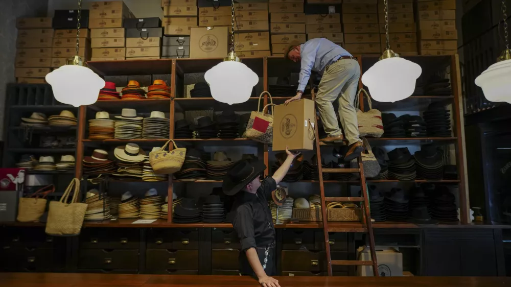 Employees work together to store products on a top shelf at the "Donde Golpea el Monito" hat shop and museum that preserves a hat-making tradition dating back to 1915, in Santiago, Chile, Thursday, April 3, 2025. (AP Photo/Esteban Felix)