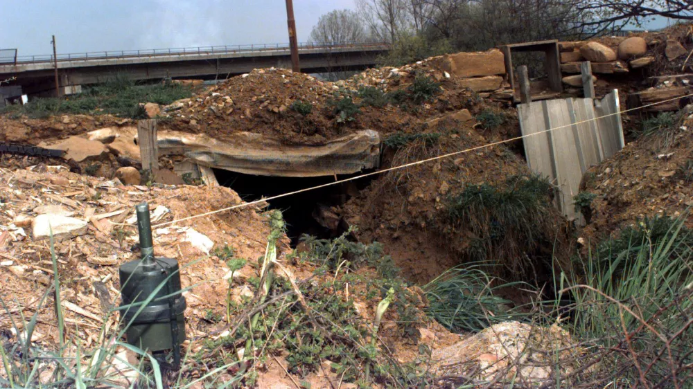 A medium close up view of a Former Yugoslavia stake mounted IMP anti-personnel mine placed near a damaged section of road, with a very visible trip wire.
