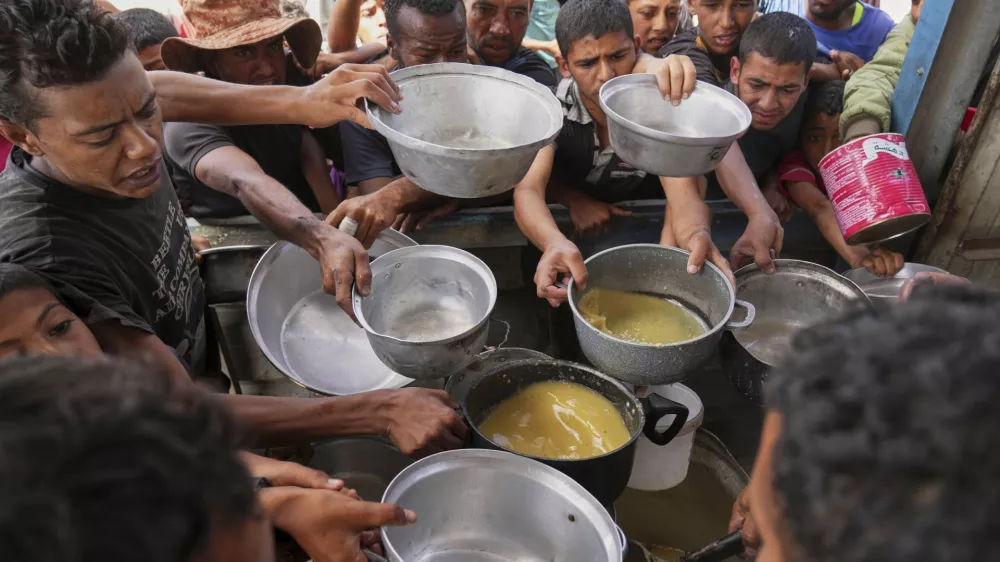 Palestinians struggle to receive cooked food distributed at a community kitchen in Khan Younis, southern Gaza Strip, Wednesday, May 14, 2025. (AP Photo/Abdel Kareem Hana)